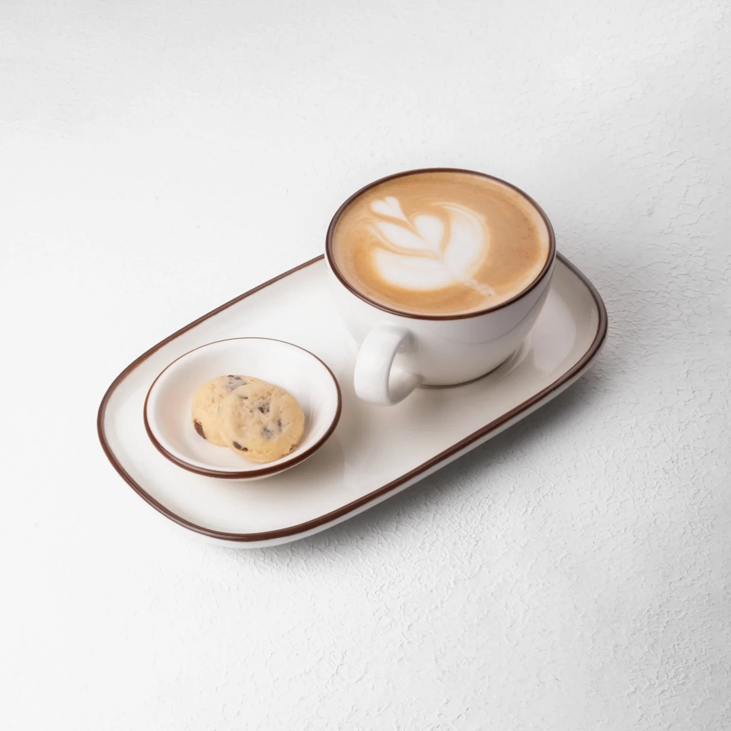 Oval tabak üzerinde kurabiye ve latte art ile sunulan kahve